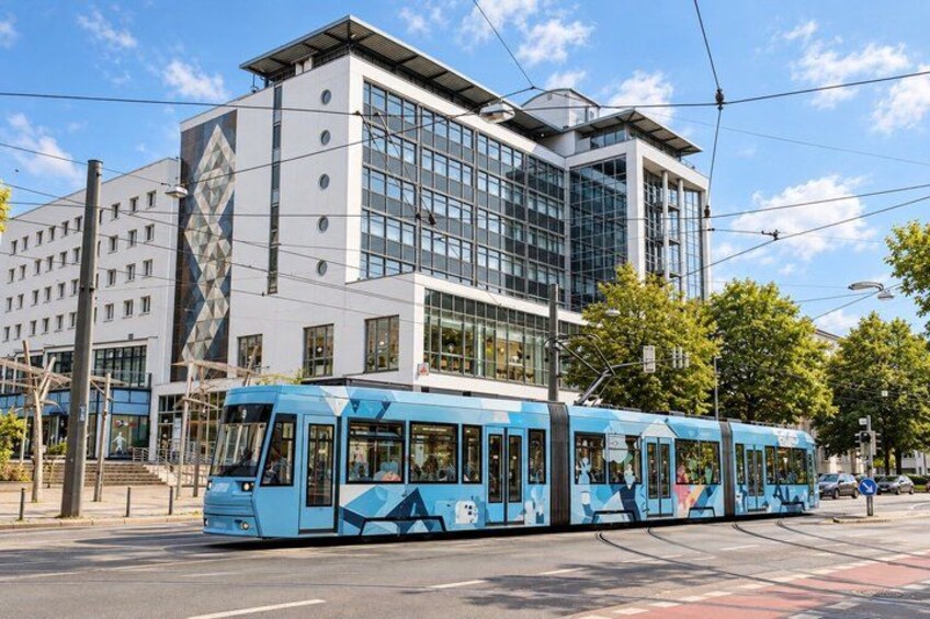 A blue tram on a city street, a modern building with glass windows, and a clear blue sky. 3