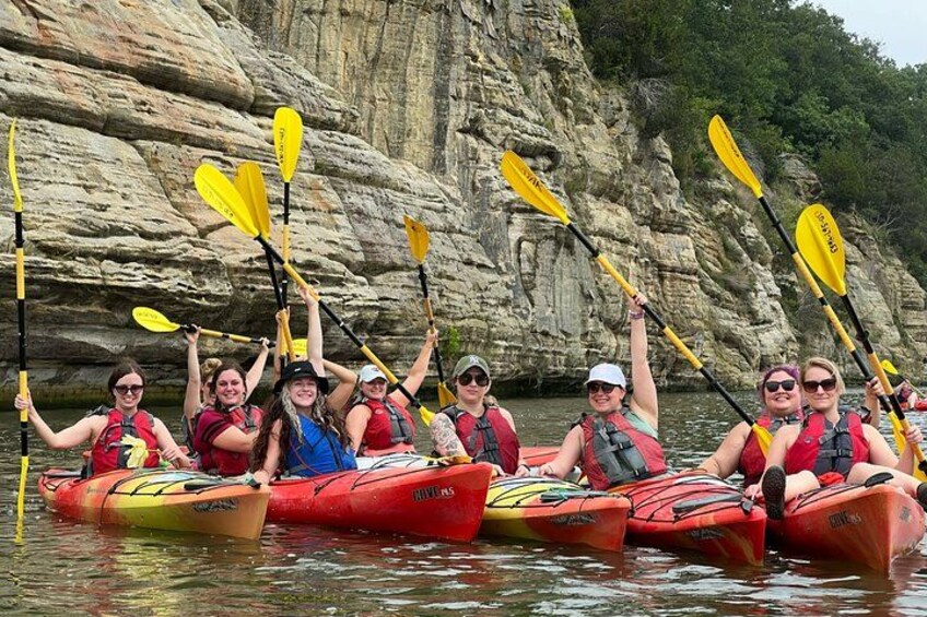 A group of people kayaking in red kayaks with yellow paddles, surrounded by rocky cliffs and water. 1