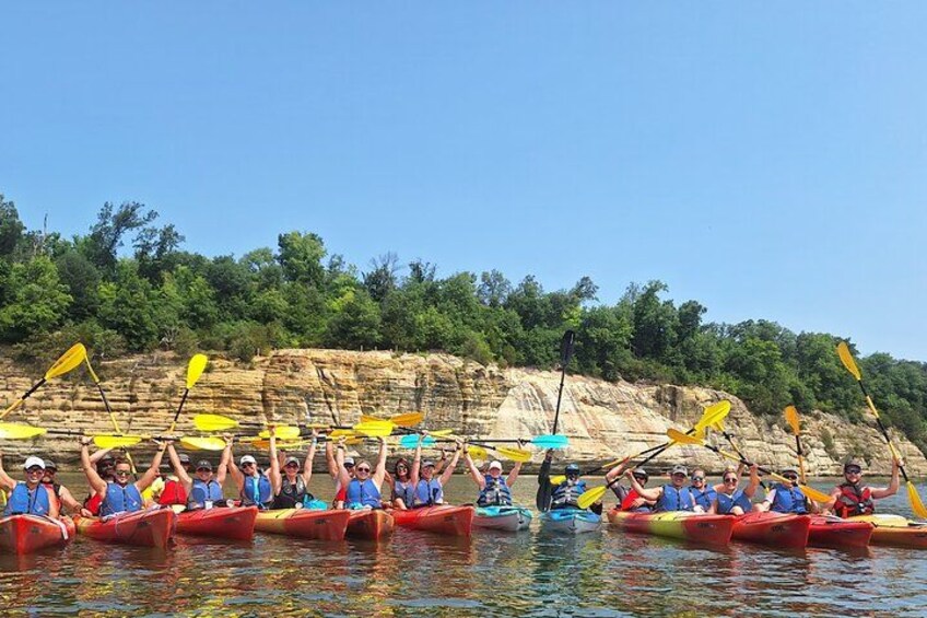 A group of people in red kayaks paddling on a river with a rocky cliff in the background. 4