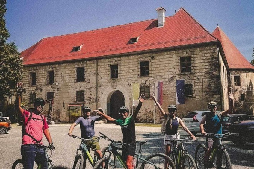 A group of cyclists in front of a historic building with a red roof. 1