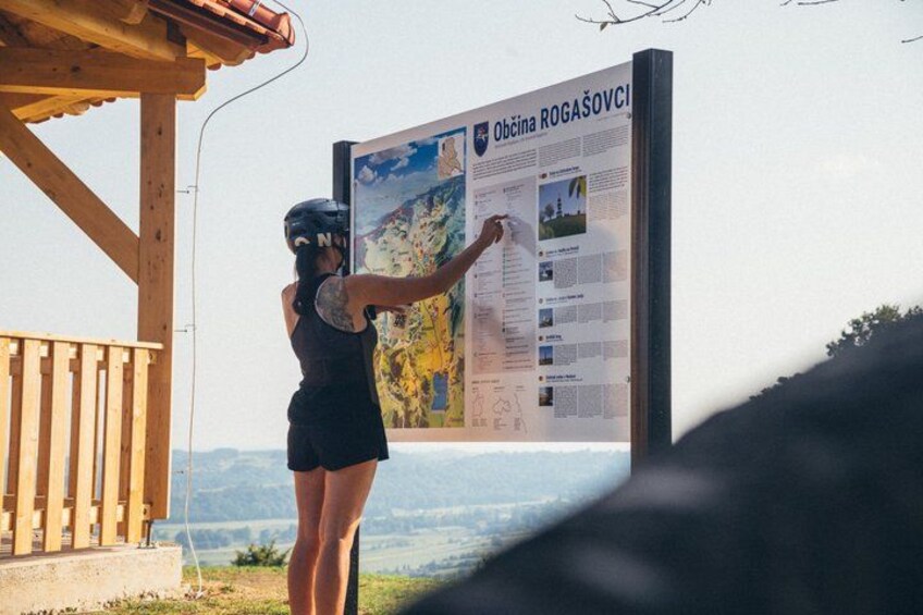 A person pointing at a large informational sign about Rogašovci. 2