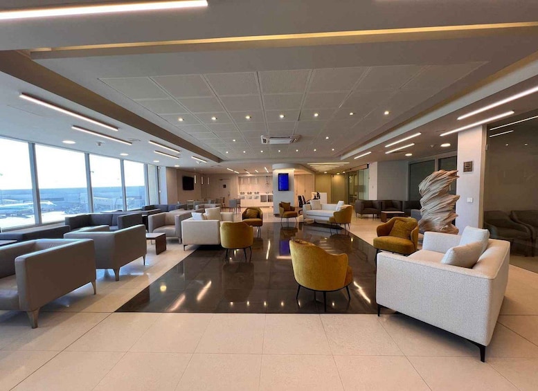 A modern lounge area with sofas, chairs, and a large window overlooking an airport. 2