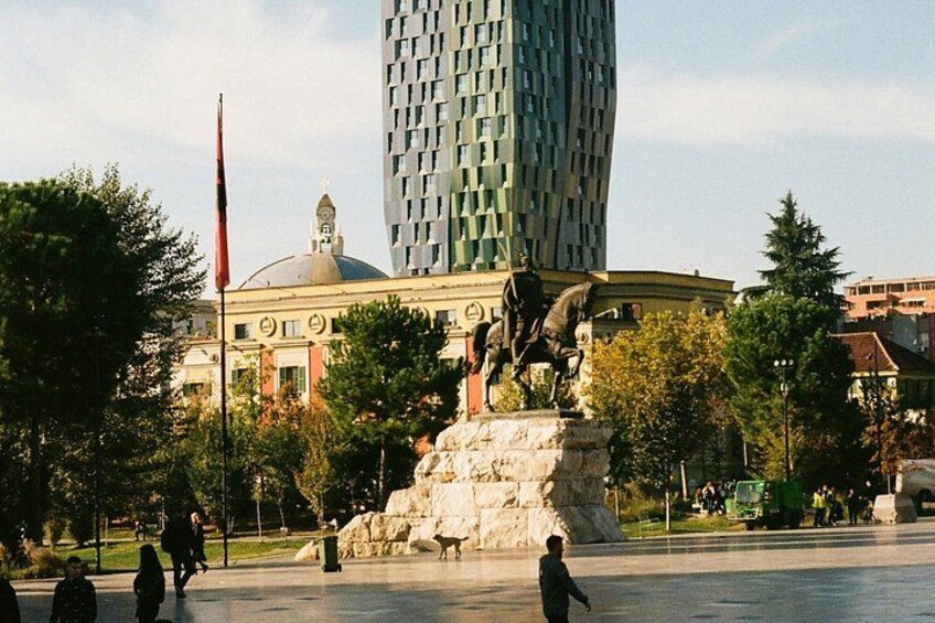 A public square with a statue, a tall building, and a flag. 5
