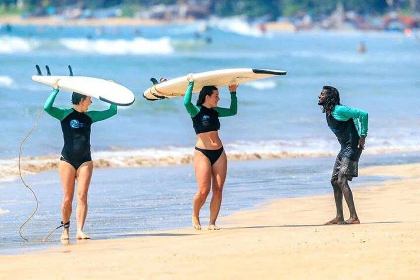 Three people on a beach, each carrying a surfboard. 4