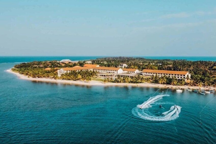 A coastal resort with a large building, palm trees, and a clear blue sea. 3