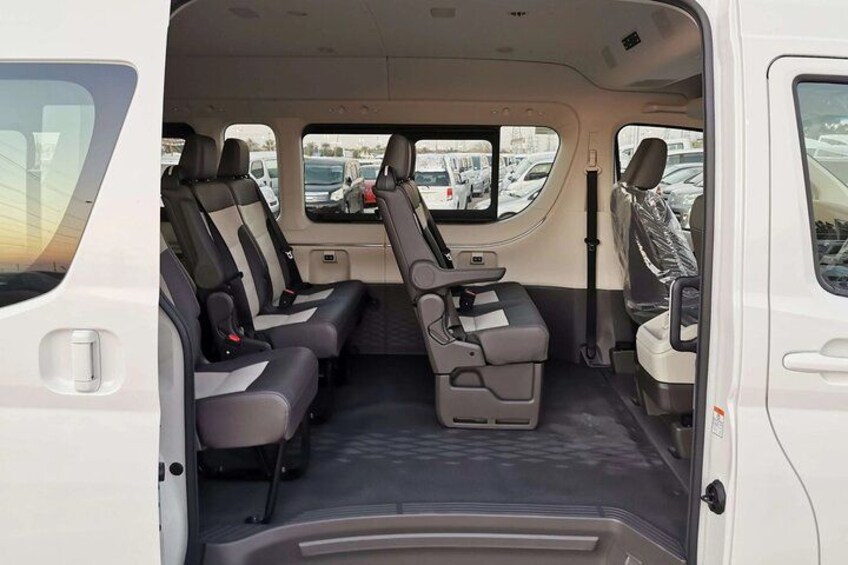 A white van interior with grey seats, a central aisle, and a rear view mirror. 5