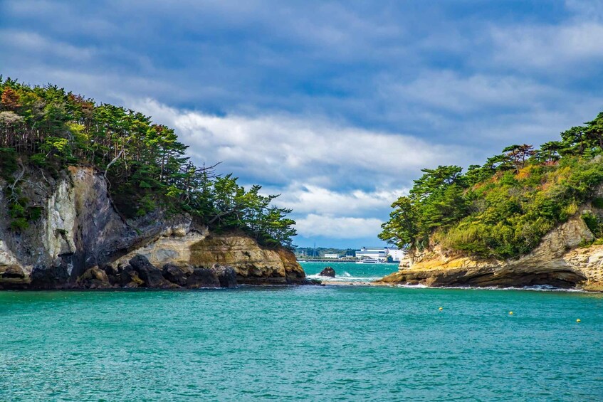 Paisaje costero con acantilados rocosos, agua turquesa cristalina y una vista distante de un barco y edificios. 5