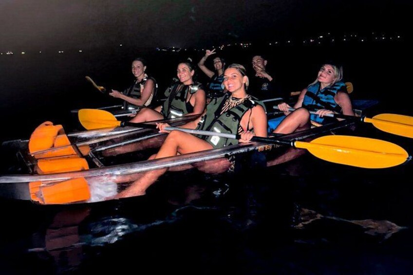 A group of people in a boat with yellow paddles, wearing life jackets, on a body of water at night. 1