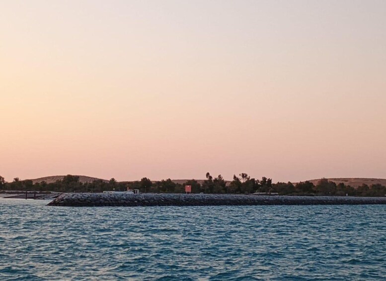 A calm sea at sunset with a rocky breakwater and distant hills. 1