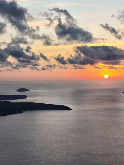 A sunset over a calm sea with scattered clouds and distant landforms. 2