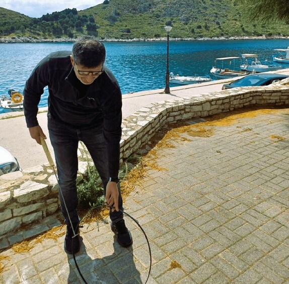 A man cleaning a stone pathway by a body of water with boats in the background. 5