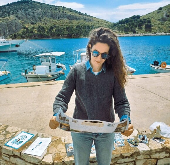 A person reading a map at a harbor with boats and a hilly landscape in the background. 4