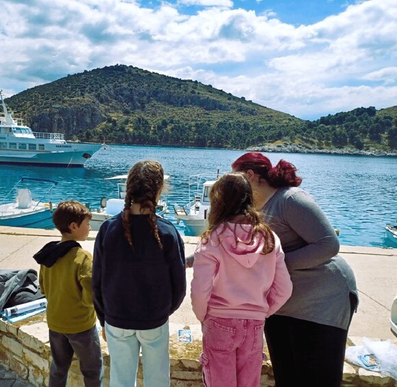 A group of people standing by a dock, overlooking a body of water with boats and a hilly landscape in the background. 3