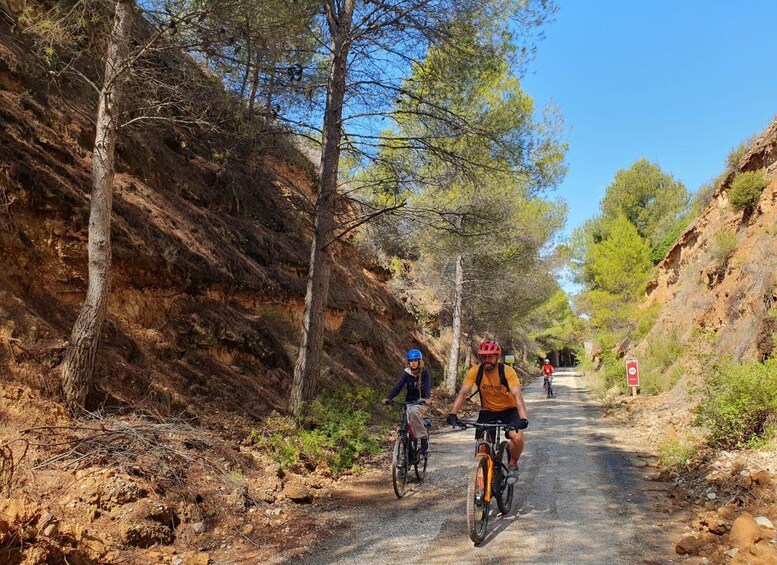 A dirt road with cyclists, surrounded by rocky terrain and sparse vegetation. 1