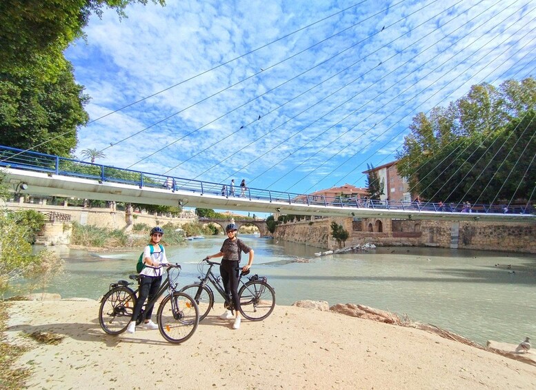 A river with a bridge, cyclists, and a sandy beach. 2