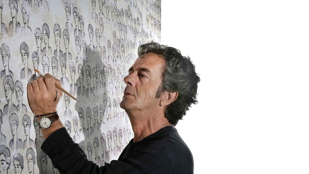 A person painting a wall with repeated portraits. 1