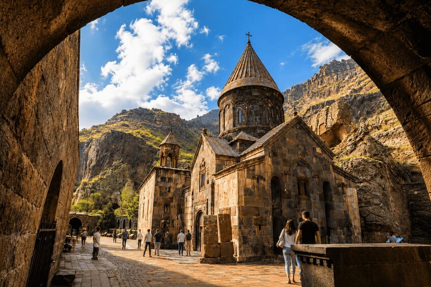 A historic stone church with a bell tower and dome, surrounded by rugged mountains and a clear sky. 3