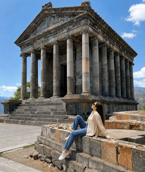 A classical building with columns, a person sitting on steps, and a mountainous landscape in the background. 5