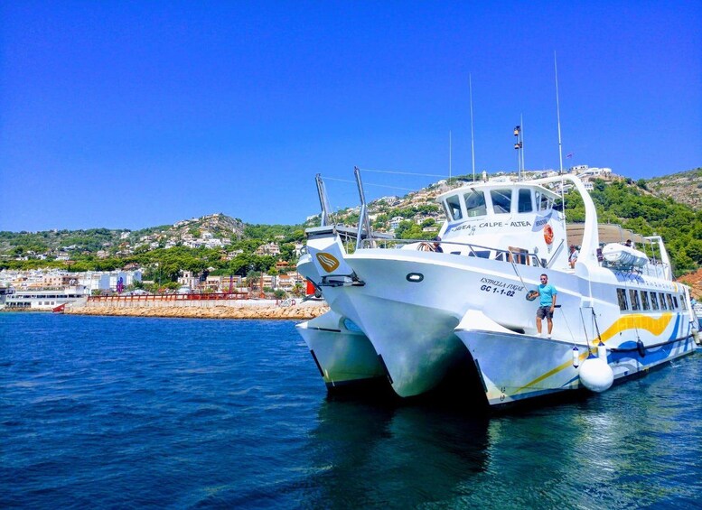 Un barco blanco con detalles azules y amarillos amarrado en un puerto con una colina al fondo. 1