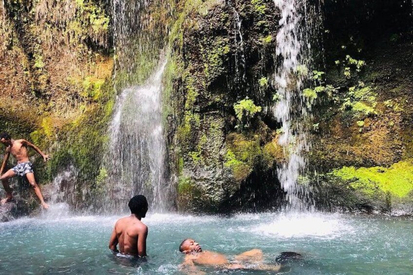 A waterfall, clear water, and people swimming. 1