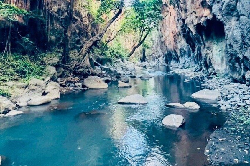 A river with clear water, rocks, and a rocky cliff. 4