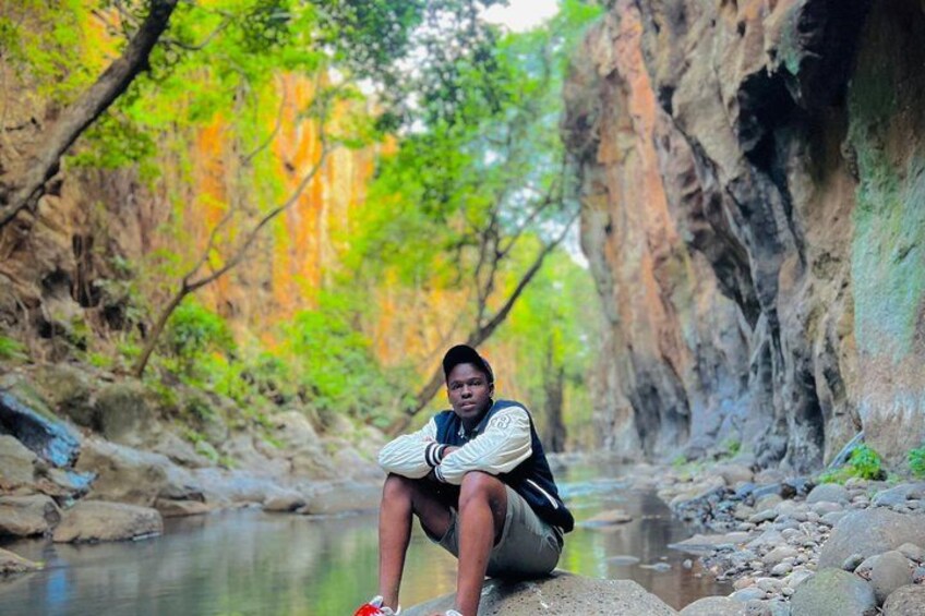 A person sitting on a rock by a river in a rocky canyon with trees. 5