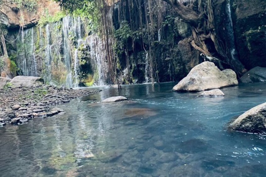 A clear river with rocks, a waterfall, and large boulders in a forested area. 2