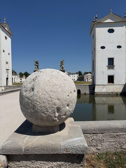 A large stone sphere in a courtyard with classical architecture, including statues and a building with a dome. 3