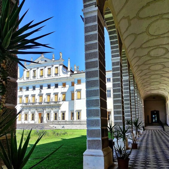 A grand building with classical architecture, a covered walkway with columns, and a well-maintained lawn. 1