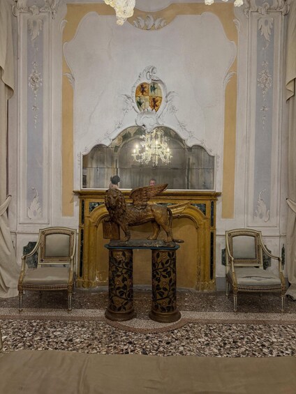 An ornate room with a large mirror, two chairs, and a lion statue on a pedestal. 2