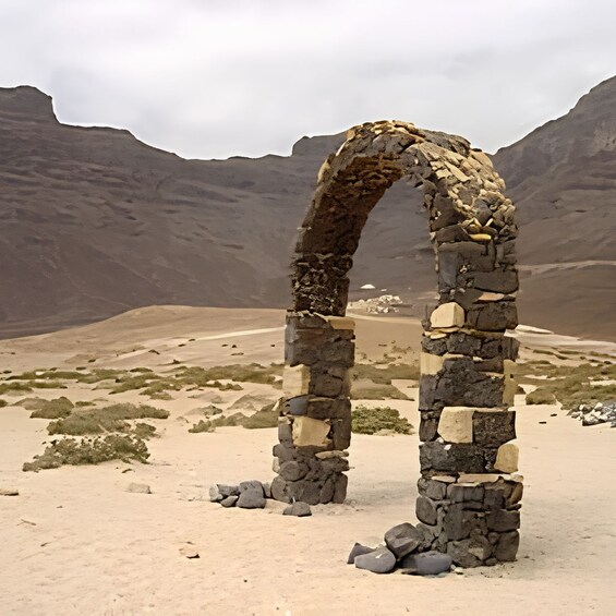A stone archway in a desert landscape with mountains in the background. 1