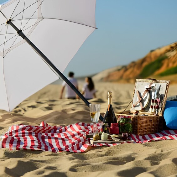 A picnic setup on a sandy beach with a checkered blanket, a bottle of wine, a glass, and a basket with food and a bicycle. 3