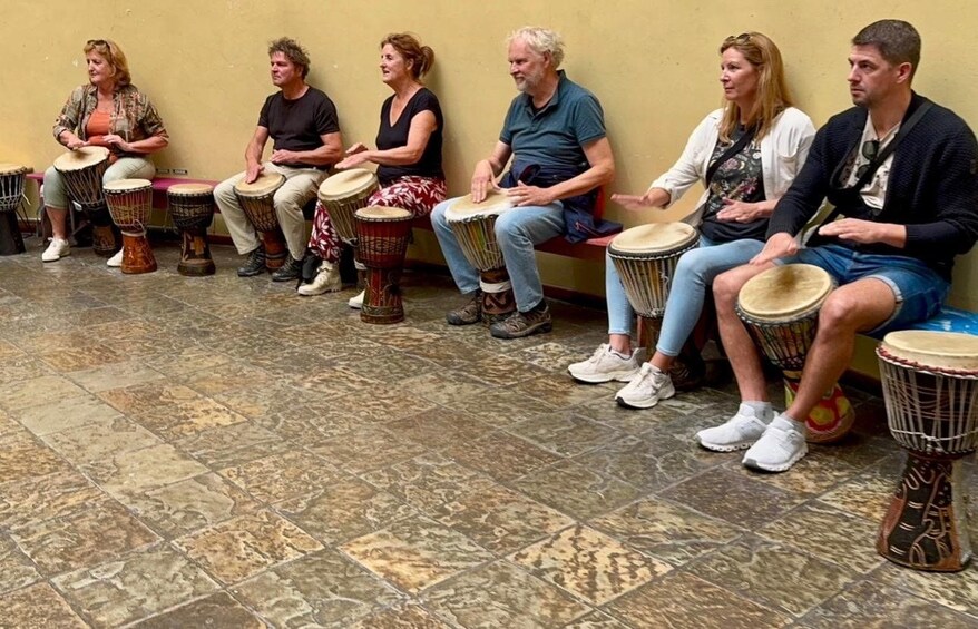 A group of people seated on a bench, each playing a drum. 2