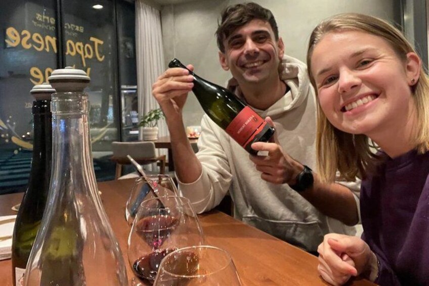 Two people sitting at a table with wine bottles and glasses. 1