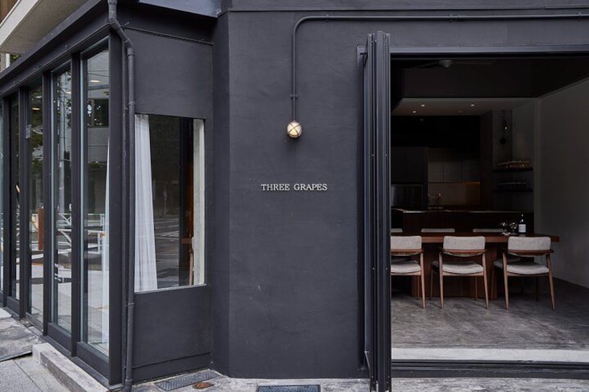 A modern building with a dark facade, a glass entrance, and a sign that reads 'THREE GRAPES'. 2