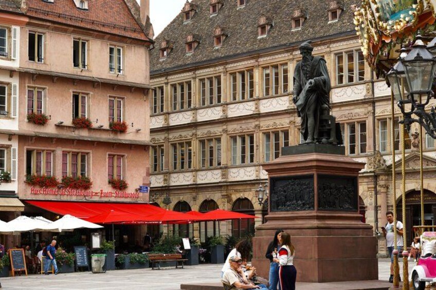 A historic building with a statue, outdoor seating, and a red awning. 5
