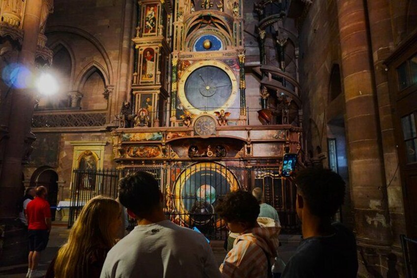 A cathedral interior with ornate decorations, a large clock, and a crowd of visitors. 1