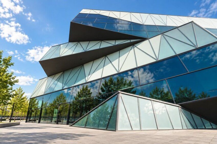 A modern glass building with geometric shapes and a clear blue sky. 4