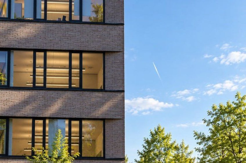 A multi-story building with large windows and a clear sky with a contrail. 3