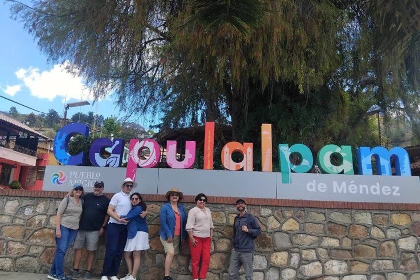 A group of people standing in front of a colorful sign with the text 'Copuialpam' and 'PUEBLO MAGICO de Méndez'. 3