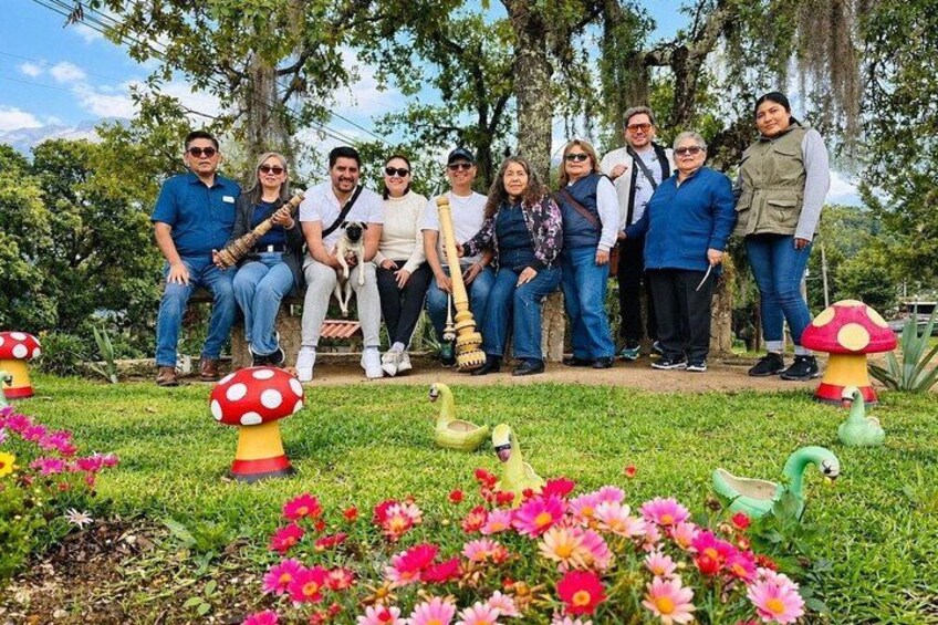 A group of people sitting on a bench in a garden with colorful flowers and decorative mushroom sculptures. 1