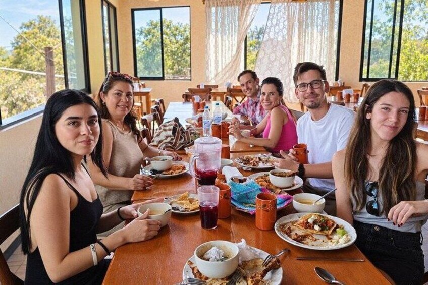A group of people dining at a wooden table with various dishes and drinks. 2