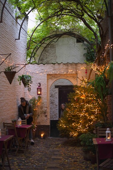 A cozy outdoor cafe with brick walls, hanging plants, and a decorated Christmas tree. 2