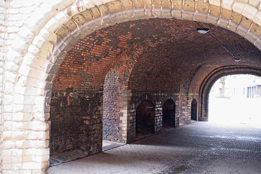 An arched brick tunnel with a cobblestone floor and a hanging light fixture. 3