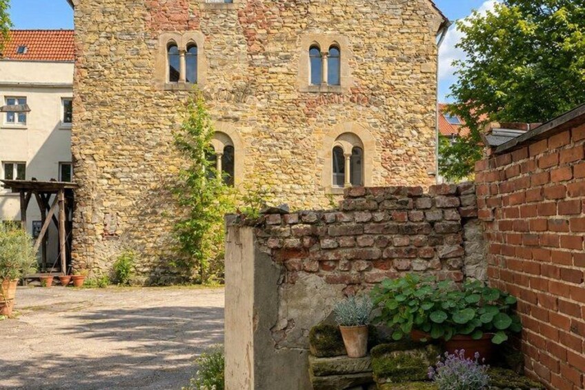 A stone building with arched windows, a brick wall, and potted plants. 2