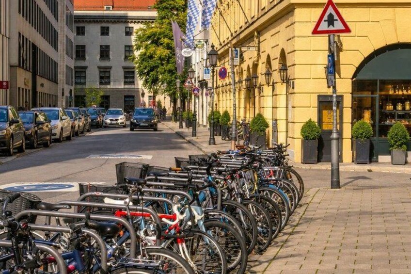 A row of bicycles parked on the sidewalk, a building with a yellow facade, and a pedestrian crossing sign. 3