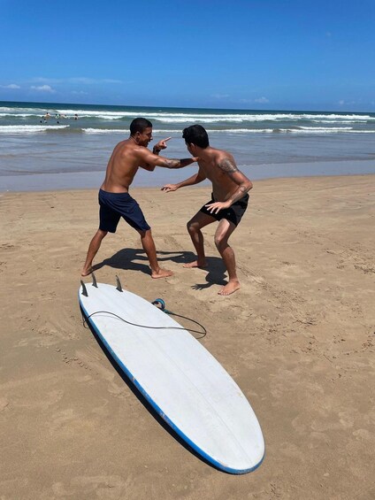 Dos hombres en una playa con una tabla de surf al frente. 4