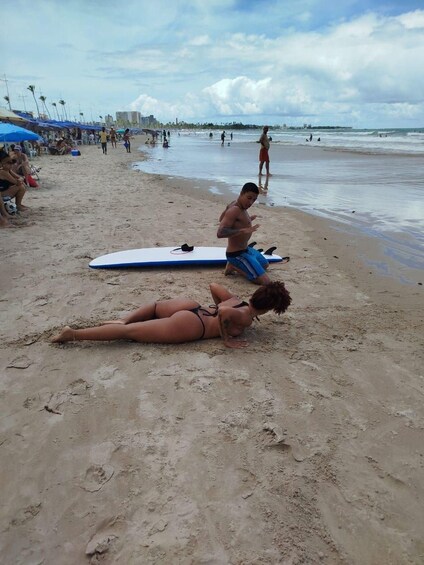 Una playa con gente tomando el sol, una tabla de surf y un horizonte urbano lejano. 2