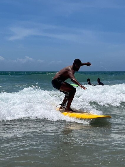 Una persona surfeando sobre una tabla amarilla en el océano, con olas. 1
