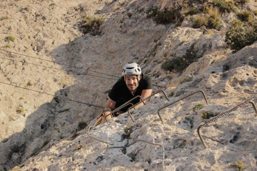 A person climbing a rocky slope with metal handholds. 4